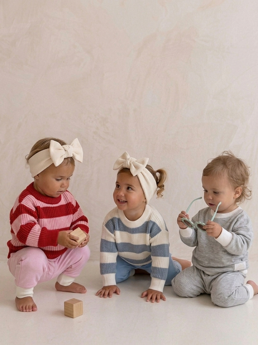 Three children in colorful outfits sitting on a white floor.