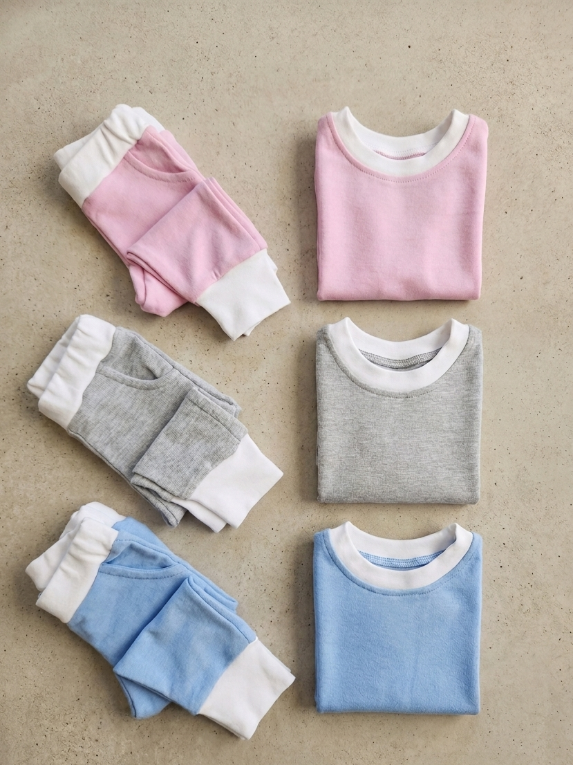 Set of folded pajama sets in pink, gray, and blue on a beige background