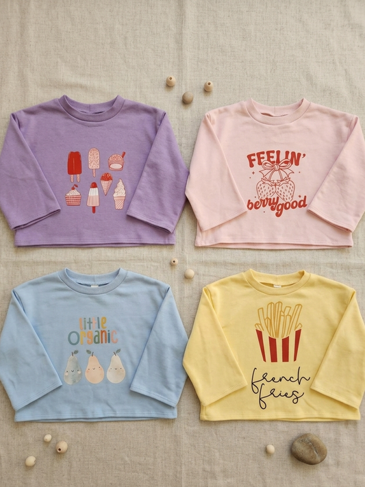 Four children's sweatshirts in purple, pink, blue, and yellow with various prints on a textured surface.